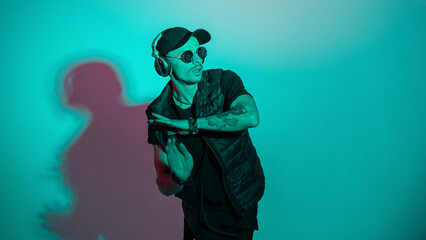 Man dancer in fashion outwear listening to music and dancing in studio with creative cyan and pink light