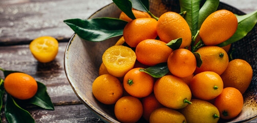 Fresh kumquat in bowl on wooden background