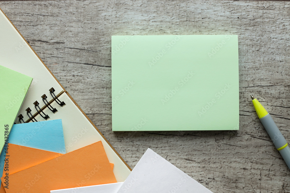 Poster sticky note on wood table. next to a pen and a notepad with a spring on the table.