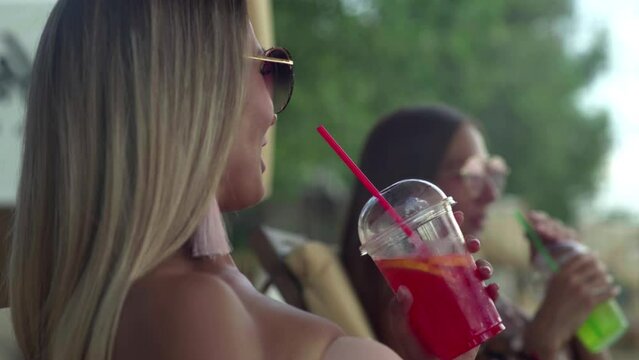 Two young women on the beach sunbathing and drinking cocktails