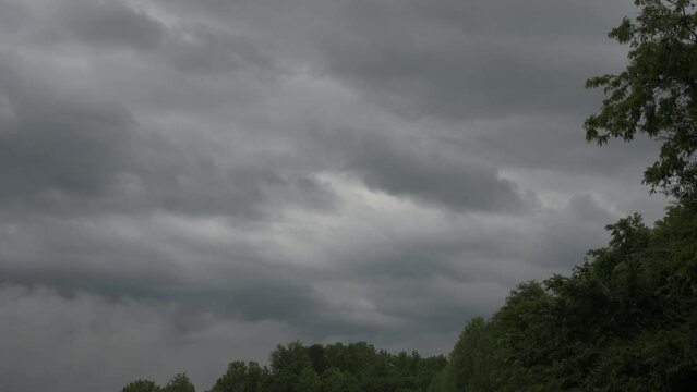 Dark clouds fill the sky afront a green forest of trees in Spring timelpase form.