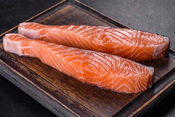 Fresh salmon fillets on black cutting board with herbs and spices