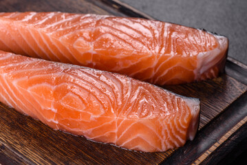 Fresh salmon fillets on black cutting board with herbs and spices