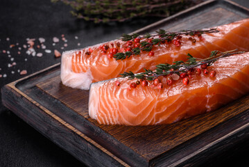 Fresh salmon fillets on black cutting board with herbs and spices