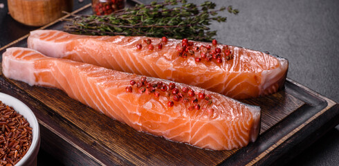 Fresh salmon fillets on black cutting board with herbs and spices