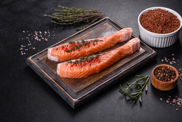 Fresh salmon fillets on black cutting board with herbs and spices