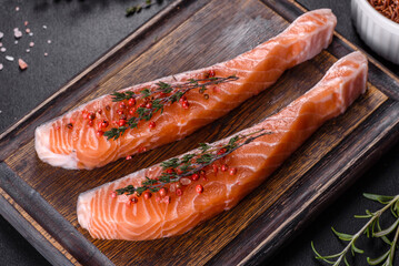 Fresh salmon fillets on black cutting board with herbs and spices