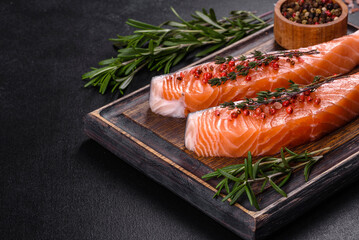 Fresh salmon fillets on black cutting board with herbs and spices