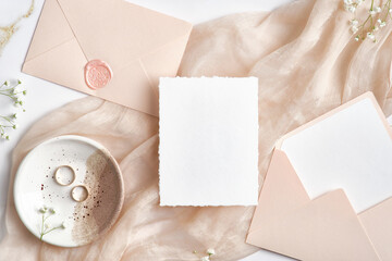 Wedding invitation card mockup, wedding envelopes, rings on beige cloth. Flat lay, top view.