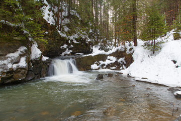 Small waterfall  in winter mountain forest in snow