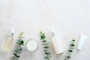 Transparent cosmetic bottles, tube, jar of cream with eucalyptus leaves on stone table. Natural,...