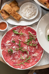 Traditional Beef Carpaccio Garnished with Parmesan Cheese and Fresh Arugula Leaves
