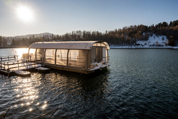 Panoramic lake vessel anchored on the shore of snow covered Bajer lake, lit by the gentle, winter sun at the town of Fuzine, Croatia