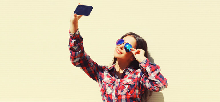 Portrait of beautiful young woman taking selfie by smartphone on white background