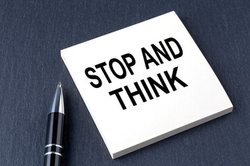 STOP AND THINK text on the sticker with pen on the black background