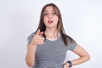 Shocked young Arab woman wearing striped t-shirt over white background  points at you with stunned expression