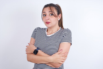 young Arab woman wearing striped t-shirt over white background shaking and freezing for winter cold...