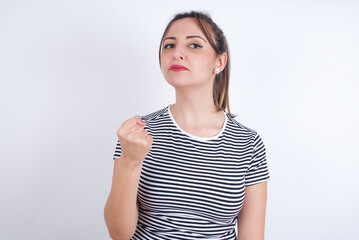 young Arab woman wearing striped t-shirt over white background shows fist has annoyed face...