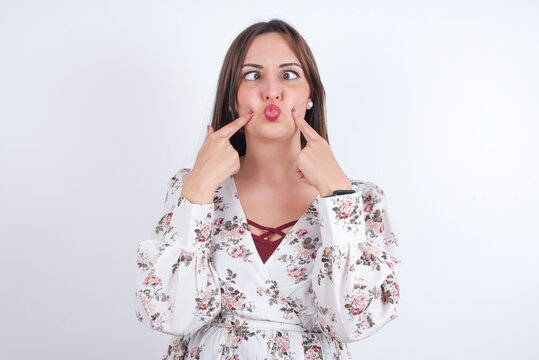 young Arab woman wearing floral dress over white background  crosses eyes and makes fish lips funny grimace
