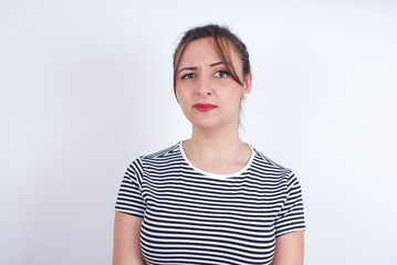 Fototapeta premium Displeased young Arab woman wearing striped t-shirt over white background frowns face feels unhappy has some problems. Negative emotions and feelings concept