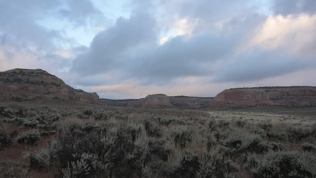Fast moving Utah cloud time-lapse above grassy bushes field with small moon at sunrise.