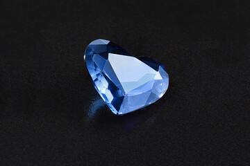 Faceted precious stone, in the form of a heart, on a black textured background, close-up.