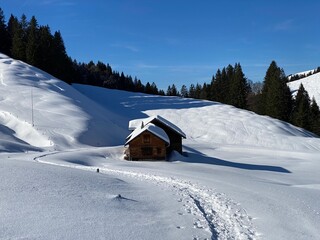 Fototapeta na wymiar Idyllic Swiss alpine mountain huts dressed in winter clothes and in a fresh snow cover on slopes on the Alpstein mountain range - Mountain pass Schwägalp, Switzerland (Schweiz)