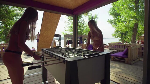 Women playing table football or kicker with miniature players on the beach in bathing suits