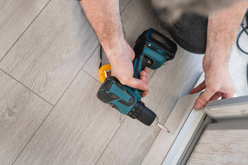 One unknown man caucasian male using electric cordless screwdriver drill assembling furniture at home DIY carpenter at work close up on hands copy space