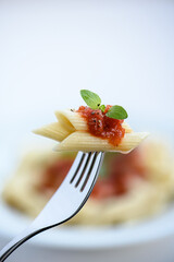 Close up Pasta Penne mit Sauce Napoli mit Basilikumblatt auf einer Gabel mit hellem Hintergrund 
