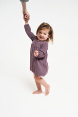 A girl dances with her mother by the hand. A cute little girl in a purple dress is learning to dance. Vertical photo with a child on a light background.