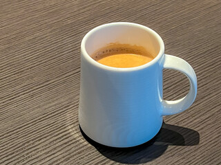 Selective focus of white coffee mug with creamy on top with warm light in cafe, Hot or warm drink in the morning on brown wooden table background.