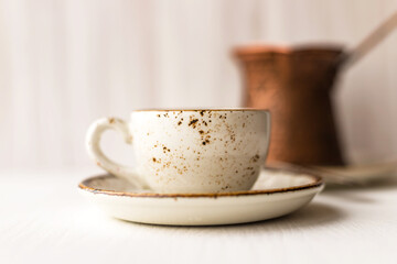 Cup of black Turkish coffee and coffee maker turk on white wooden table against wall background