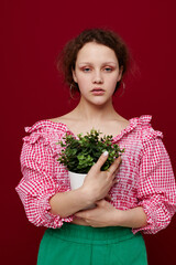 Young woman standin and holding flower in pot red background unaltered