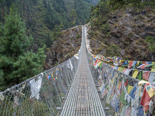 chain bridge with prayer flags between two banks in valley Khumbu in Nepal