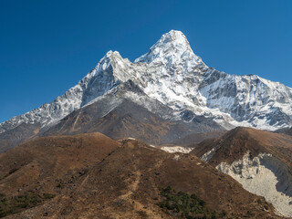 view to mount Ama-Dablam through brown hills in summer day under blue sky in Nepal