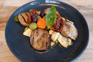 Mixed vegetable dish on a plate including chargrilled aubergine, courgettes with carrots and olives along with sun dried tomatoes.