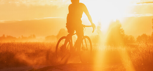 Silhouette of a professional cyclist riding on a countryside trail with dramatic sunset background. Panoramic view. Sport an active lifestyle. © Chinart