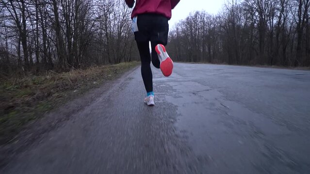 Female feet wearing sneakers running along walkway in park,  Partial view of jogger exercising outside in early autumn. Concept of fitness