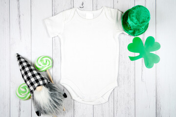Baby romper onesie product mockup. St Patrick's Day farmhouse theme SVG craft product mockup styled with green leprechaun hat and buffalo plaid gnome against a white wood background.