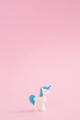 A toy white unicorn with a blue hair and a blue tail on a pink background. Poster for children's birthday. A minimal concept of fairy tales and magic.