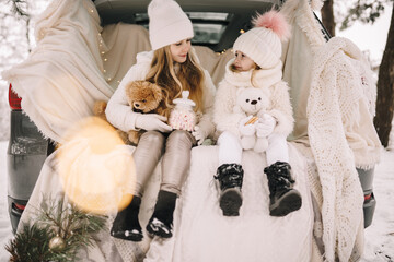 Two little girs by car in the winter forest