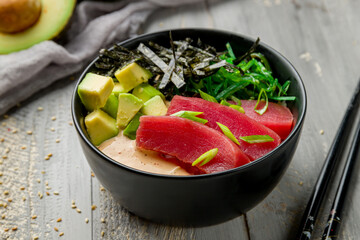 Ahi poke with tuna, avocado, chukka and sauce with rice on black bowl on grey wooden table macro close up