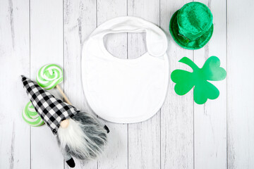 Baby bib product mockup. St Patrick's Day farmhouse theme SVG craft product mockup styled with green leprechaun hat and buffalo plaid gnome against a white wood background.