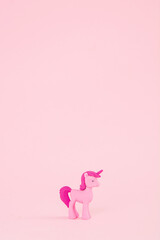 A toy pink unicorn with a pink hair and tail on a pink background. Poster for children's birthday. A minimal concept of fairy tales and magic.