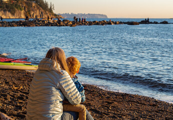 A woman and a child at seashore on a autumn day. Small boy and his mother are embracing at the seashore watching sunset