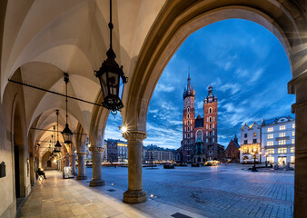 Naklejka na ściany i meble Krakow main square with view on St mary's basilica under illuminated gothic arches during overcast blue hour