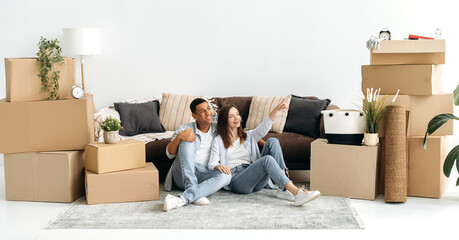 Happy spouses planning interior design of new home. Excited joyful mixed race couple in love,...