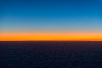 Fototapeta premium Sunrise from the window of the plane. The horizon is colored by the orange light of the sun. The first rays of the rising sun.