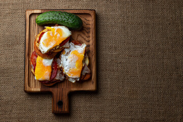 Homemade sandwiches with meat, potatoes, tomato, cucumber and fried egg on a wooden board
